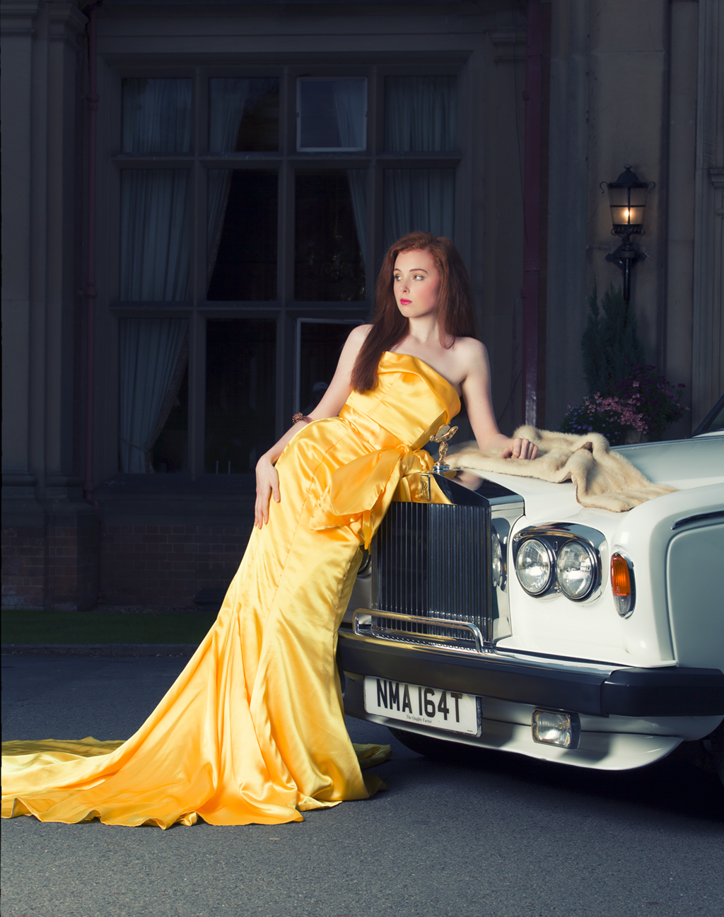 luxurious gold fall of the dress and the red of the models hair drape over a Rolls Royce